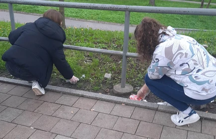 uczennice sprzątają trawnik przy chodniku