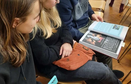 uczniowie siedzący na krzesłach i oglądający książkę