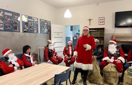 osoby przebrane za Mikołaje siedzą przy stole a jedna osoba stoi