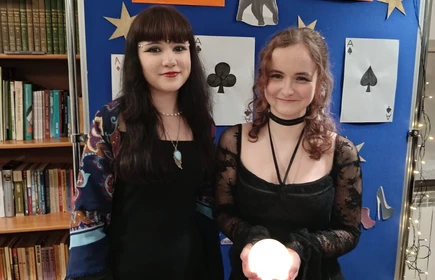 Dwie osoby dziewczyny ,stoją  za tablicą zna której są przypięte namalowane karty do wróżb