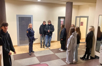 kobieta w mundurze straży miejskiej, kt&oacute;ra wygląda na osobę prowadzącą spotkanie lub prelekcję. na przeciw niej stoją młodzi ludzie chłopcy i dziewczęta  słuchający prelekcji