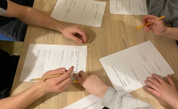 na zdjęciu widac blat drewniany na ktorym oparte są ręce uczniów a przy nich karty pracy