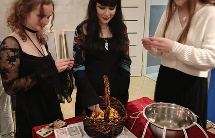 Trzy  uczennice stoją obok siebie, uśmiechnięte lub pozujące, na tle dużej niebieskiej tablicy dekoracyjnej z napisem „ANDRZEJKI”, gwiazdkami oraz ilustracjami związanymi z tradycyjnymi wróżbami.

Przed nimi stoi stół nakryty czerwonym materiałem i jasnym bieżnikiem. Na stole znajdują się przedmioty używane podczas zabaw andrzejkowych — m.in. miska z uchwytami, świeczki LED, karty, zestaw karteczek oraz kilka niebieskich kubeczków ustawionych w rzędzie.