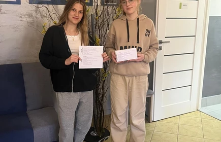 dwie młode dziewczyny  w pozycji stojącej trzymają w rękach małą białą paczkę i przekaz pocztowy
