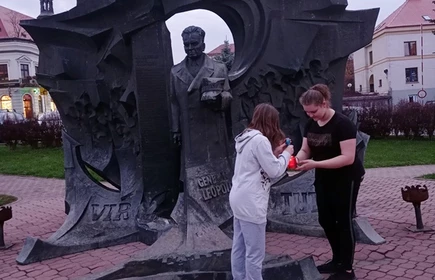 uczniowie zapalają znicz przed pomnikiem