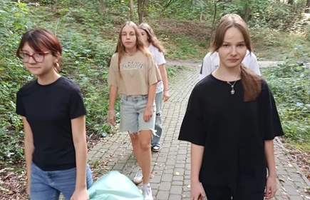 Cztery idące uczennice  zbierające śmieci z lewej uczennica trzymająca zielony worek na śmieci