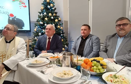 na zdjęciu widać choinkę i st&oacute;ł wigilijny przy kt&oacute;rym siedzą osoby dorosłe