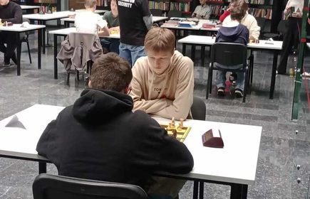 dwóch uczniów siedzących przy stoje grających w szachy