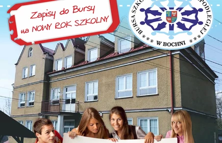  uczeń i trzy uczennice trzymajacy plakat na którym  widnieje napis z adresem i telefonem  Bursy ,za nimi widoczny jest budynek Bursy