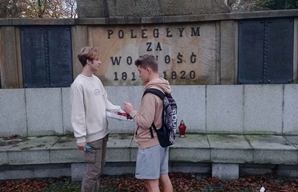 uczniowie zapalają znicz