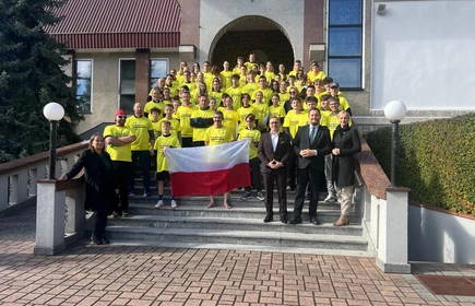 Grupa uczniów w żółtych podkoszulkach  stojących przed kościołem.