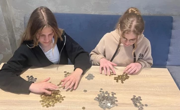 na zdjęciu widac dwie uczennice siedzace przy stole na którym są ułożone stosy  z monetami