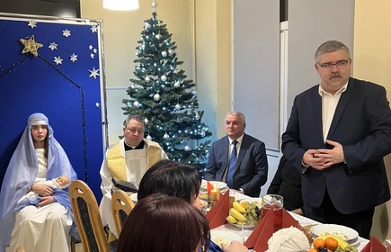 strosta przemawiający do siedzących przy stole wigilijnym