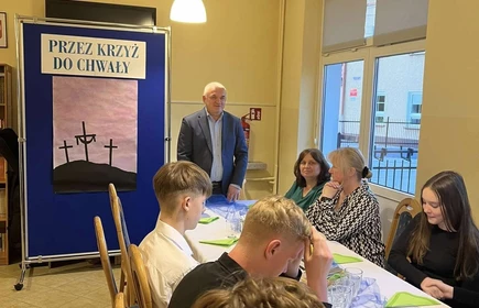 Stojacy Dyrektor Bursy szkolnej  przed siedzącymi przy wielkanocnym stole uczniami ,składa życzenia Wielkanocne