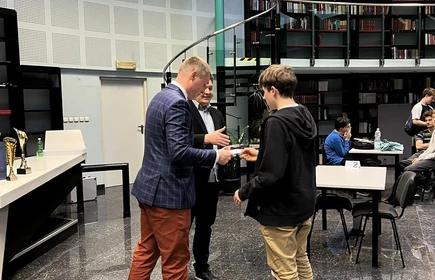 dwóch stojących uczniów  przyjmuje gratulacje od organizatora turnieju szachowego