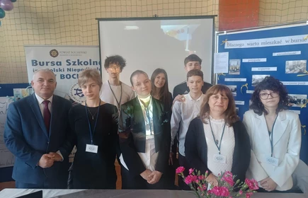 stojący uczniowie i nauczyciele  przed banerami promujacymi plac&oacute;wkę