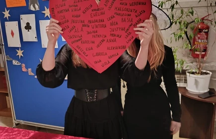 Dwie stojące osoby trzymają w rękach czerwone serce z napisami