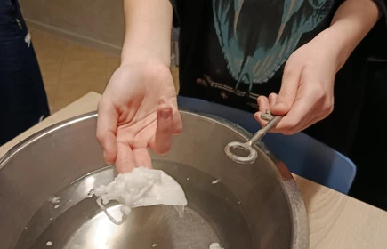 na zdęciu widoczne ręce  w prawej widoczny wosk a w lewej klucz  nad metalową miską wypełniona wodą