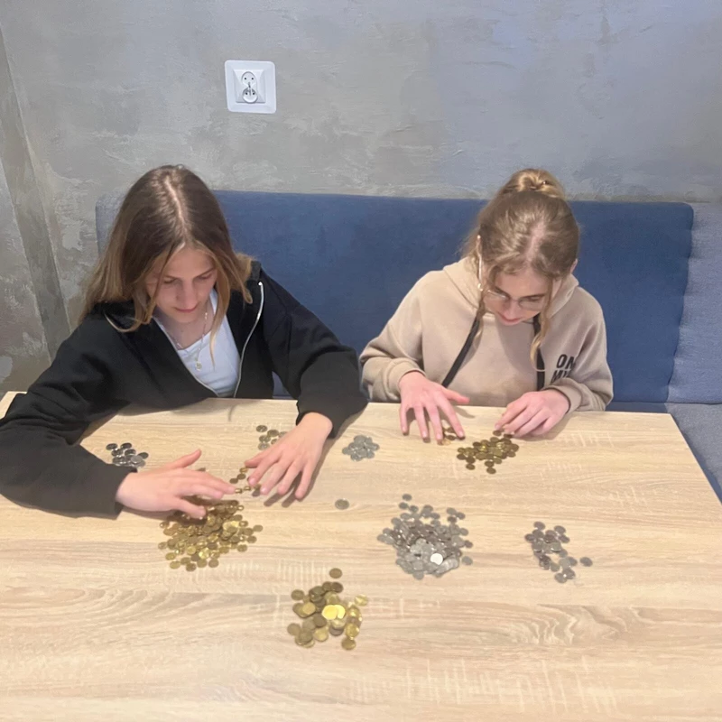 na zdjęciu widac dwie uczennice siedzace przy stole na którym są ułożone stosy  z monetami