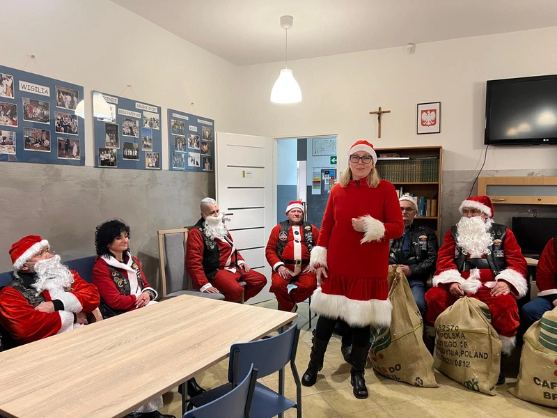 osoby przebrane za Mikołaje siedzą przy stole a jedna osoba stoi