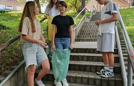 Trzy uczennice i jeden uczeń stojący na schodach zbierający śmieci
