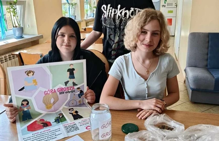 Trzy  uczennice przed blatem stołu na którym umieszczone są uzbierane grosze z Akcji Góra Grosza